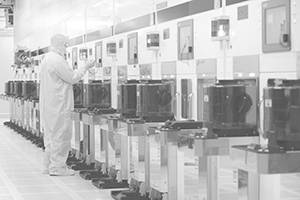 A person in a white suit operates machinery in a cleanroom facility