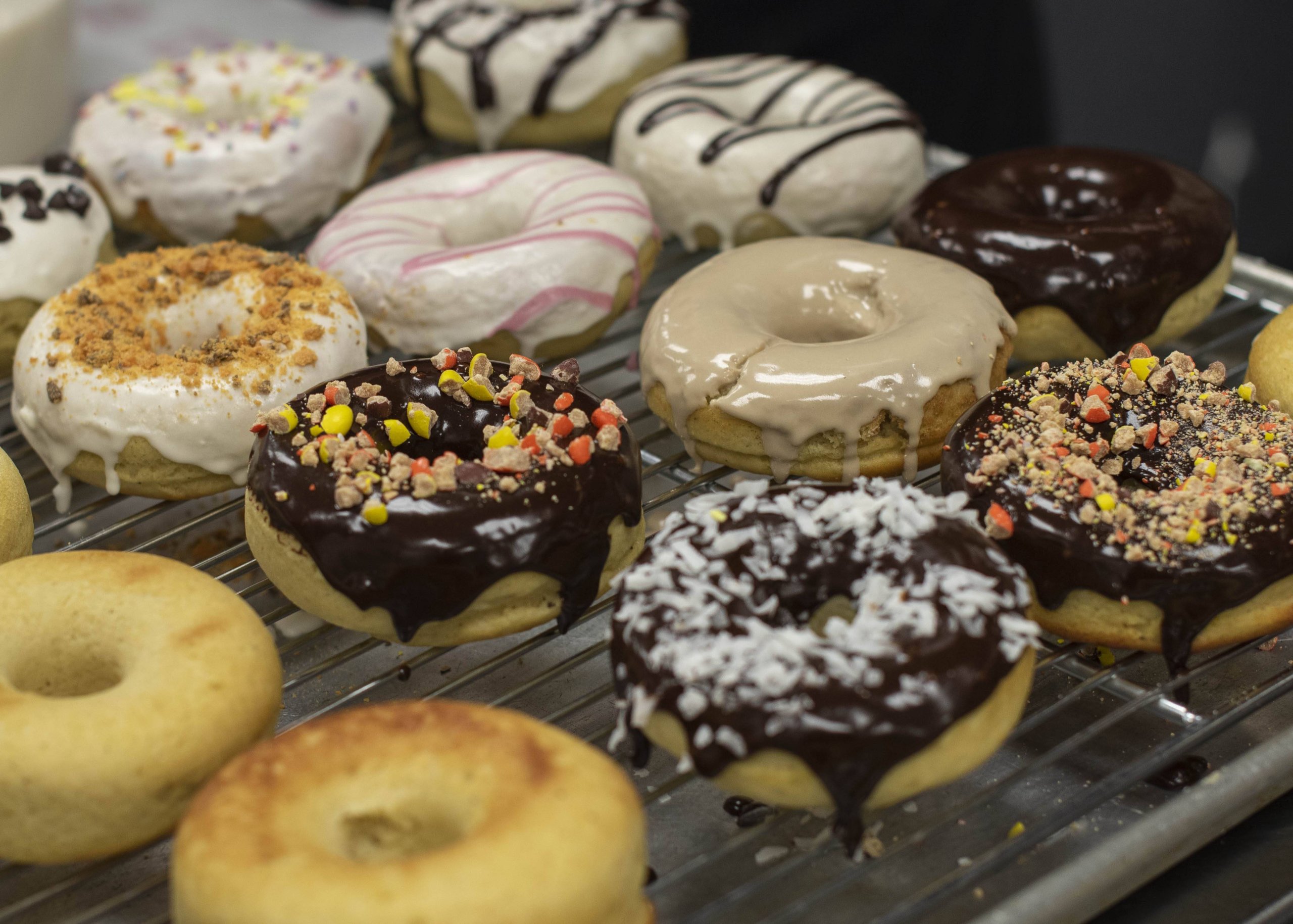 Assorted donuts with various glazes and toppings on a cooling rack