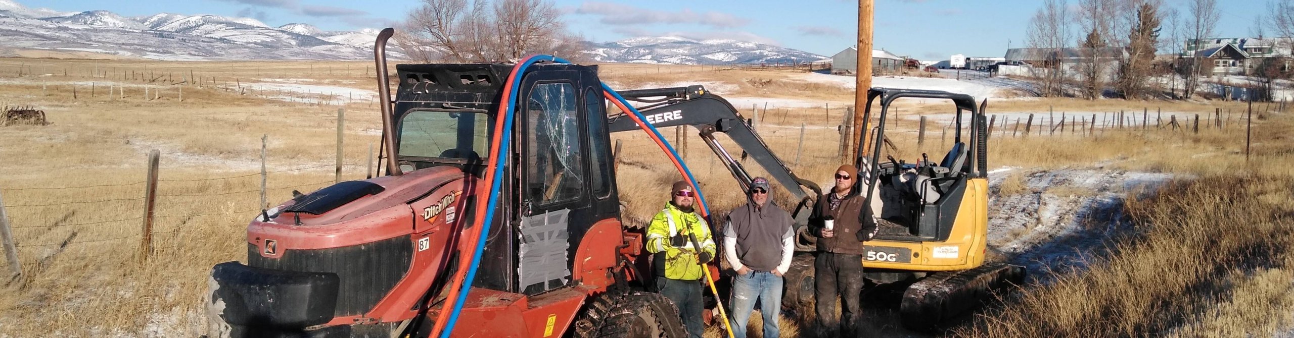 Construction workers in a snowy field with excavators and utility poles