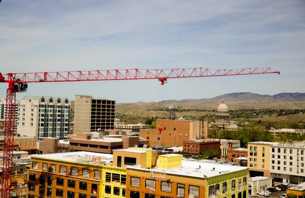 A red construction crane towers over a city skyline with various buildings under construction