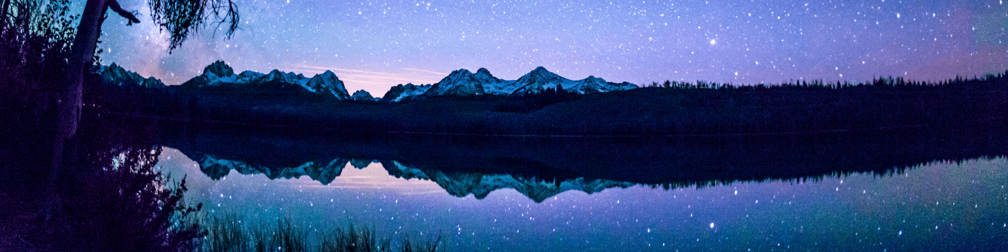 A serene night scene with a starry sky reflected in a calm lake surrounded by mountains