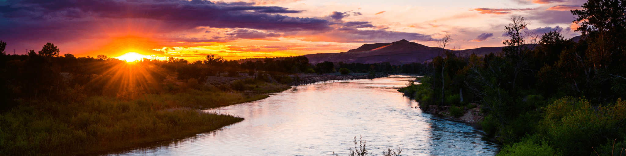 A serene river winds through a lush valley at sunset, with mountains in the distance