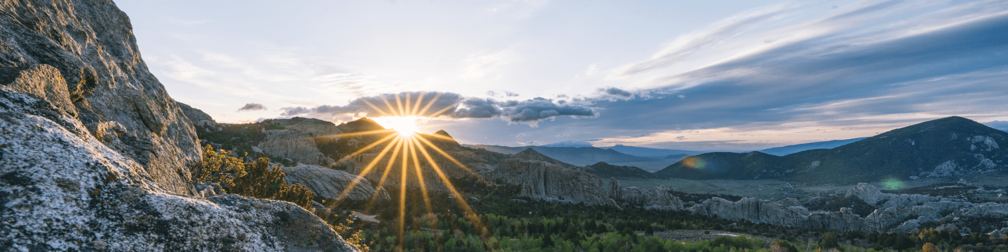 Sunrise illuminates rugged mountains and a vast valley with a rainbow effect