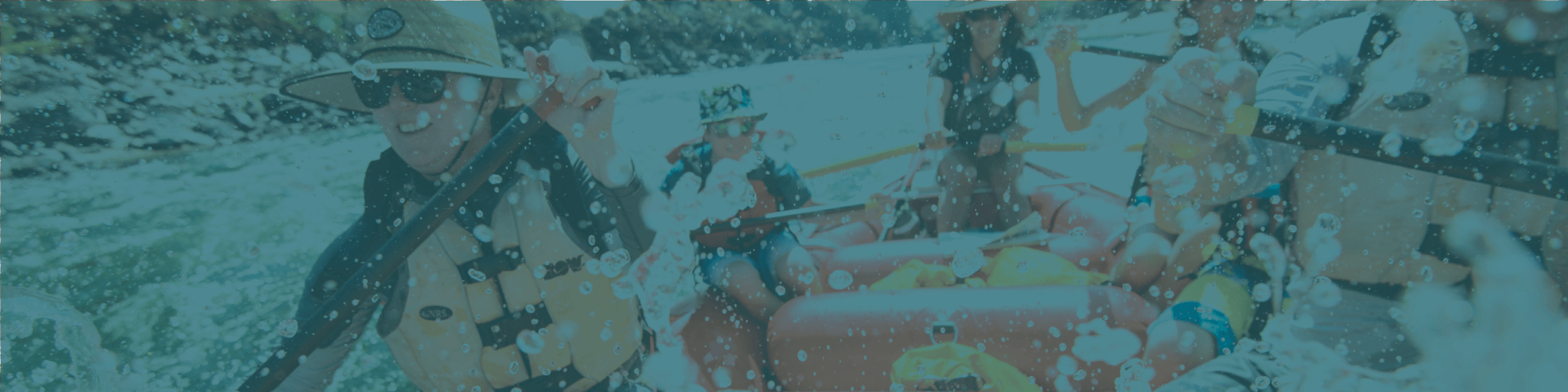 A group of people wearing life jackets and helmets are rafting down a river