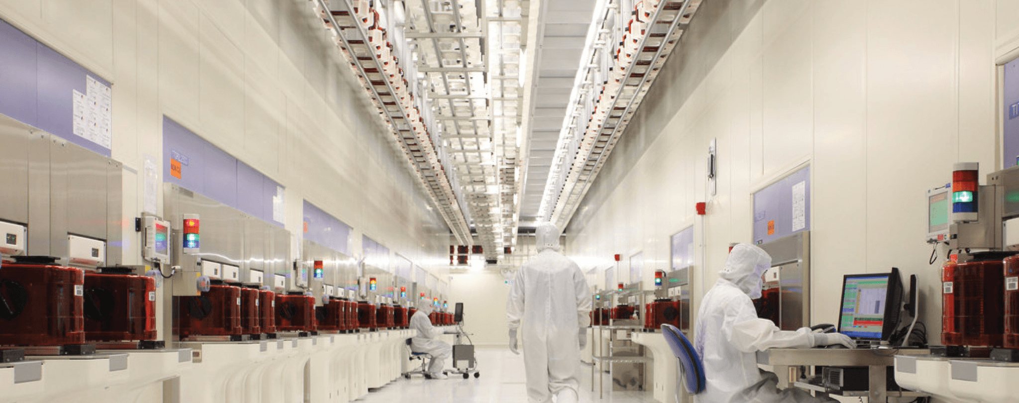 Workers in protective suits operate complex machinery in a sterile, high-tech manufacturing facility