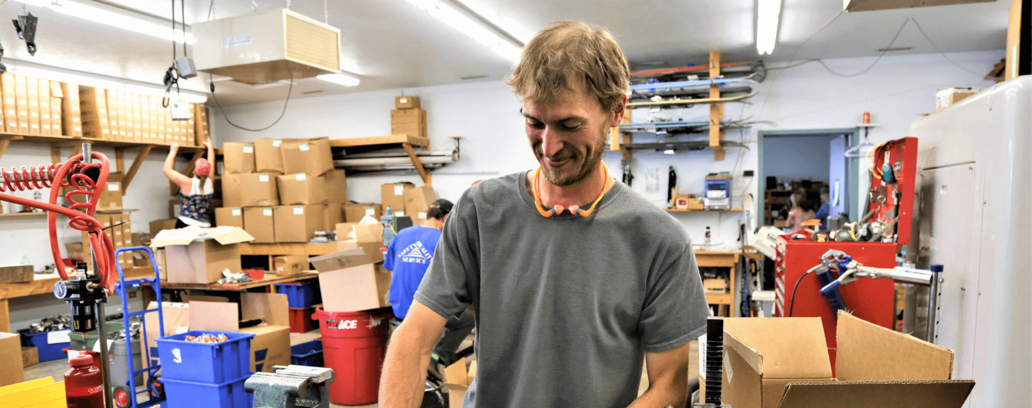Man in gray shirt works in cluttered warehouse with boxes and tools