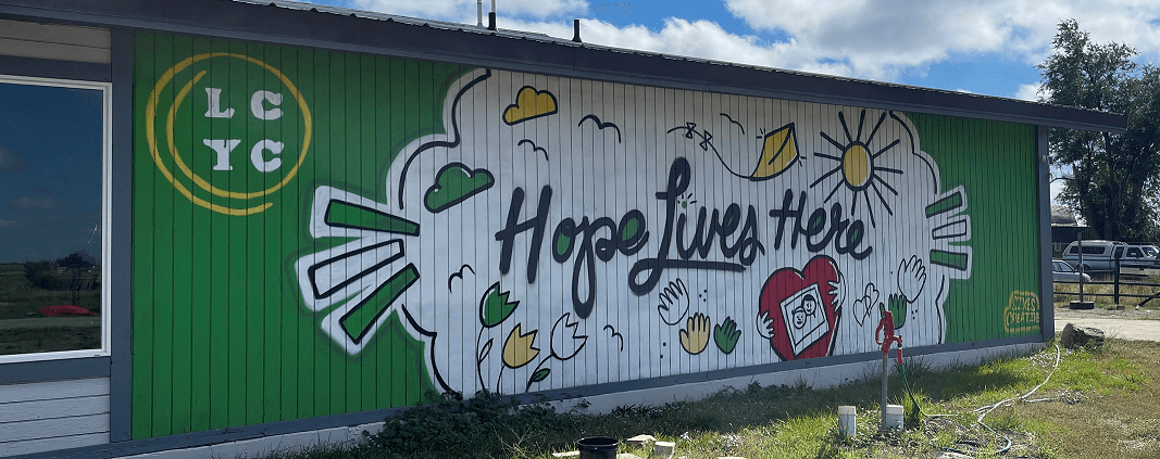 A colorful mural on a green wall features a heart, flowers, and the phrase 'Hope Lives Here'