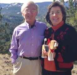 Dennis is a stately gentleman with graying hair and glasses, wearing a purple button-down shirt. Frances Conklin, with brown hair and glasses stands to his left wearing a red blouse with a black and red cardigan.