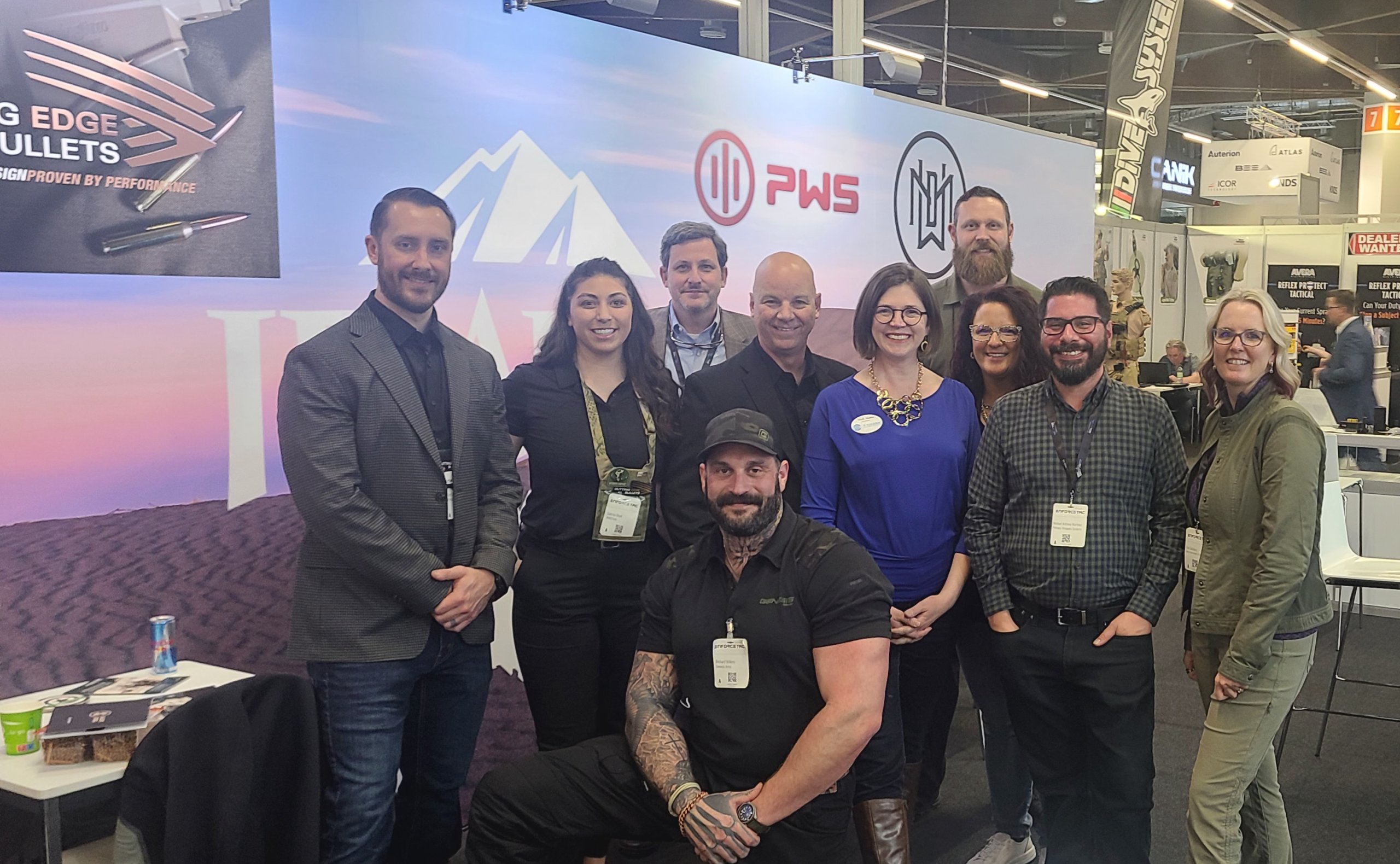 A group of ten people, including a tattooed man in the center, pose for a photo at a trade show booth