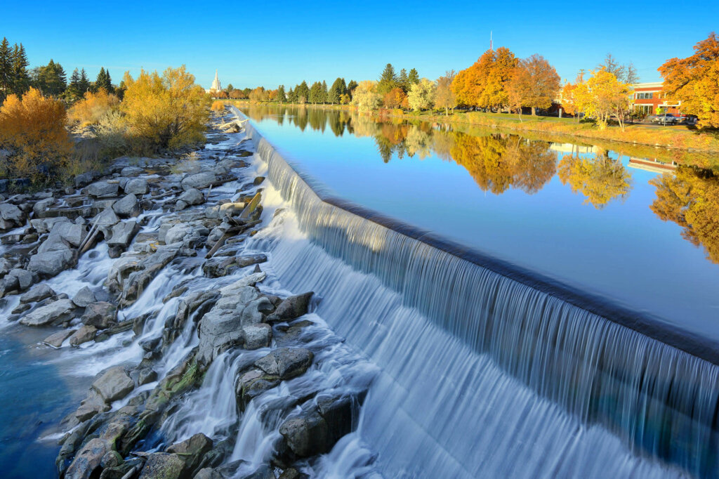 A side view of a waterfall cascading of large rocks surrounded by trees with fall colors.