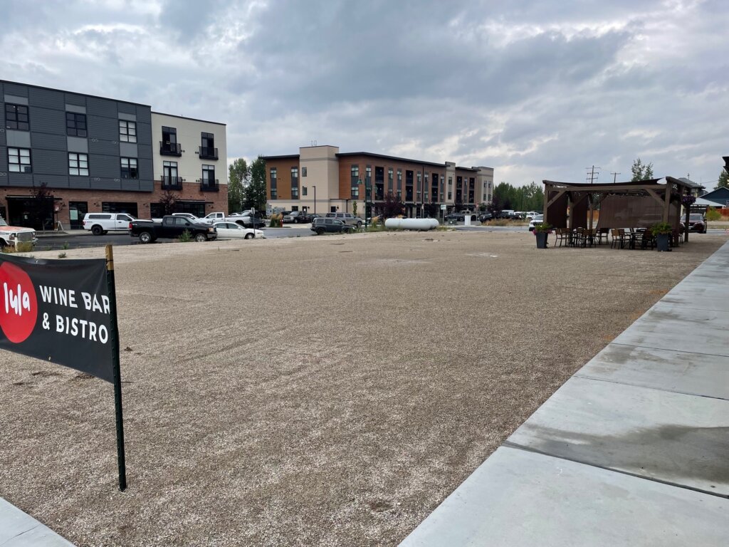 A construction site with a sign for 'Iula Wine Bar & Bistro' and a gravel parking lot in front of modern apartment buildings