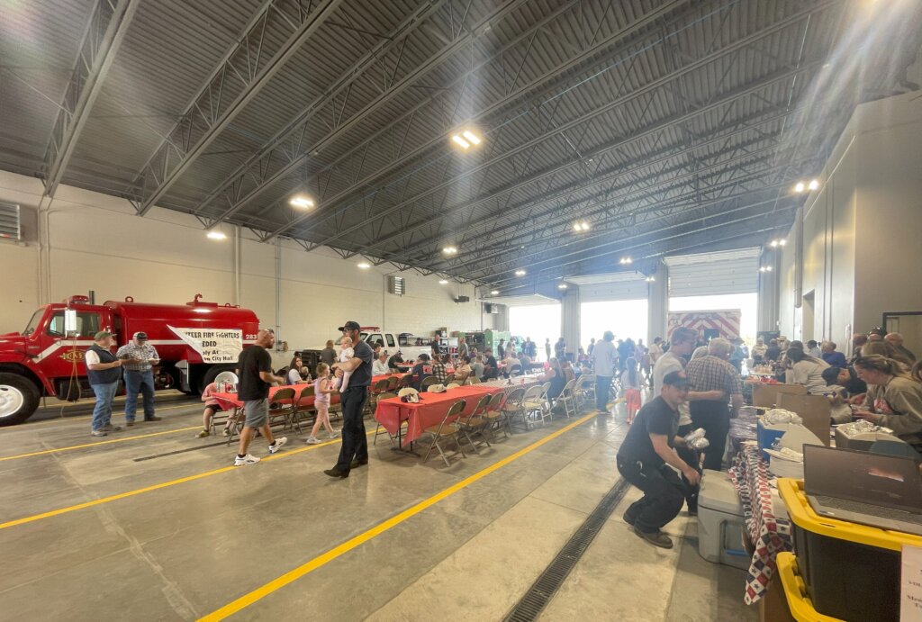 A large indoor event with a red fire truck, tables, and people gathered in a spacious hangar-like setting