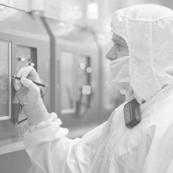 A scientist in a cleanroom suit uses a tool to work on a machine.