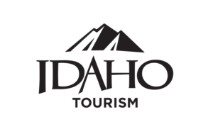 A stylized logo featuring a mountain range and the word 'IDAHO' with 'TOURISM' below