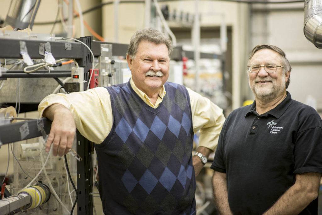 Two men stand in a laboratory filled with scientific equipment and wires