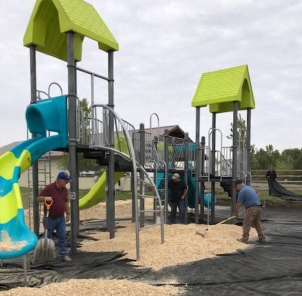 Workers install a colorful playground with slides and climbing structures on a bed of wood chips
