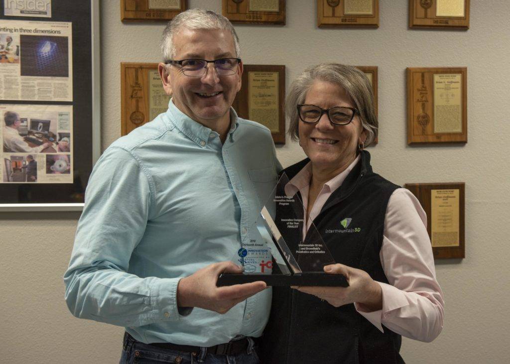 A man and woman in an office setting proudly hold an award plaque together