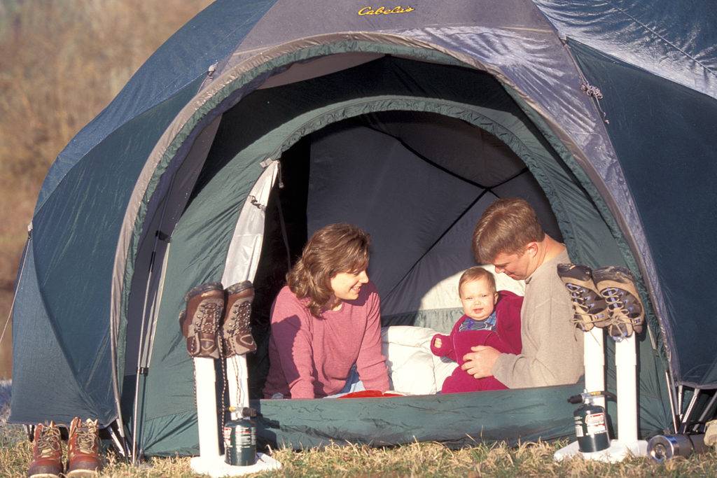 A family enjoys a camping trip in a green dome tent with their baby and hiking boots nearby