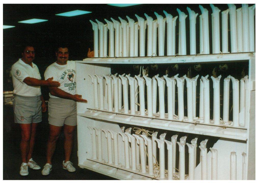 Two men stand next to a large rack filled with white cylindrical objects