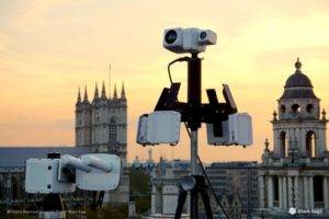 Surveillance equipment mounted on a rooftop with a city skyline in the background at sunset