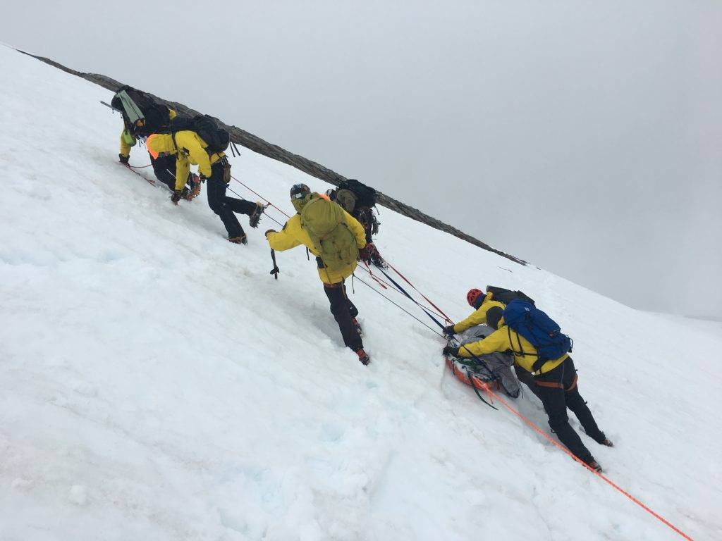 A team of climbers in yellow gear ascend a snowy mountain slope using ropes and crampons