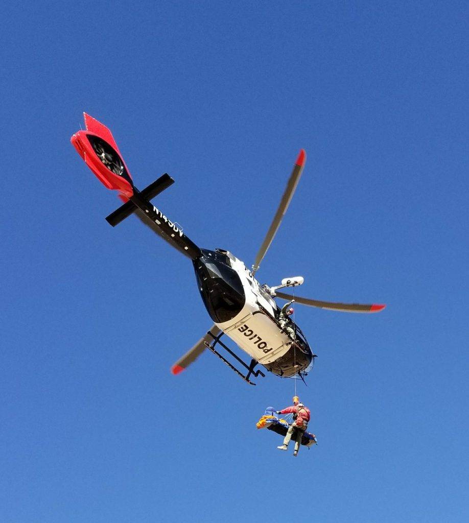 A police helicopter with a red tail rescues a person in a blue harness from the sky