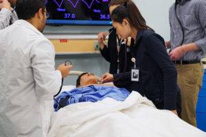 Medical students practice physical exams on a mannequin in a hospital setting