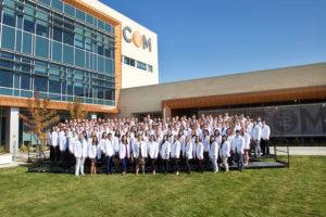 A large group of medical professionals in white coats pose for a photo in front of a modern hospital building