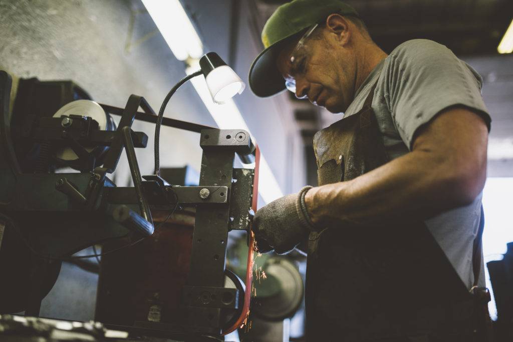 A skilled worker in a workshop uses a grinding wheel to sharpen a metal tool