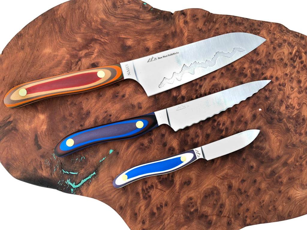 Three colorful-handled kitchen knives with wavy blades lie on a wooden cutting board