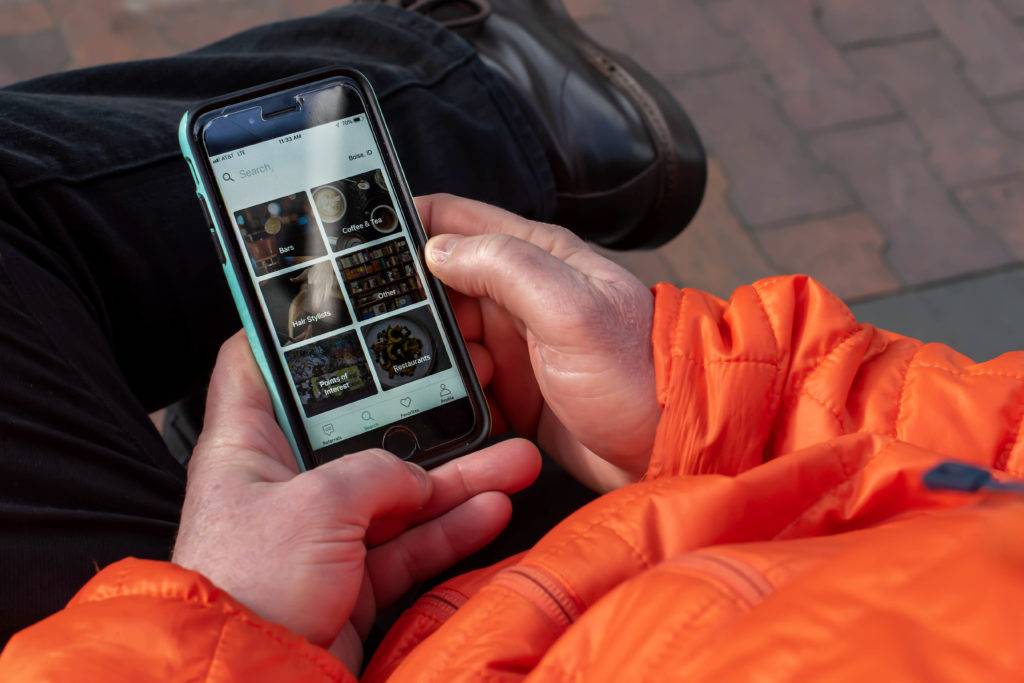 A person wearing an orange jacket holds a smartphone displaying a food ordering app