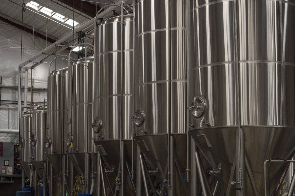 A row of large, shiny stainless steel fermentation tanks in a brewery