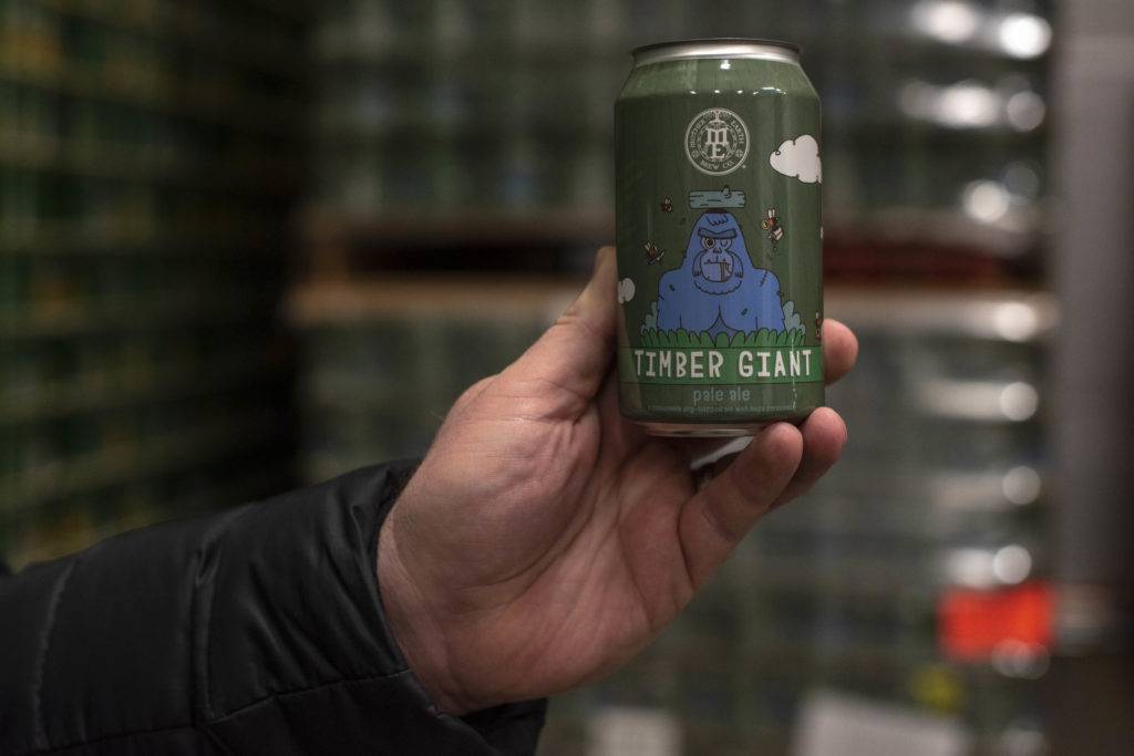 A hand holds a green can of Timber Giant Pale Ale with a cartoon gorilla on it