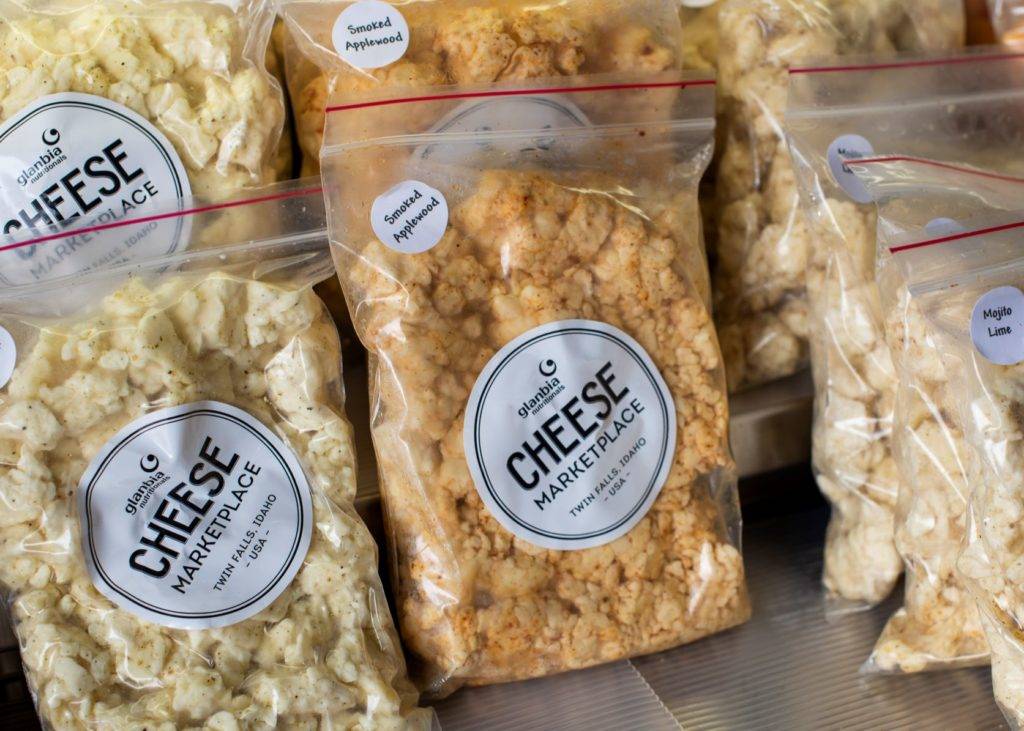 Clear plastic bags filled with various types of cheese curds are displayed on a shelf
