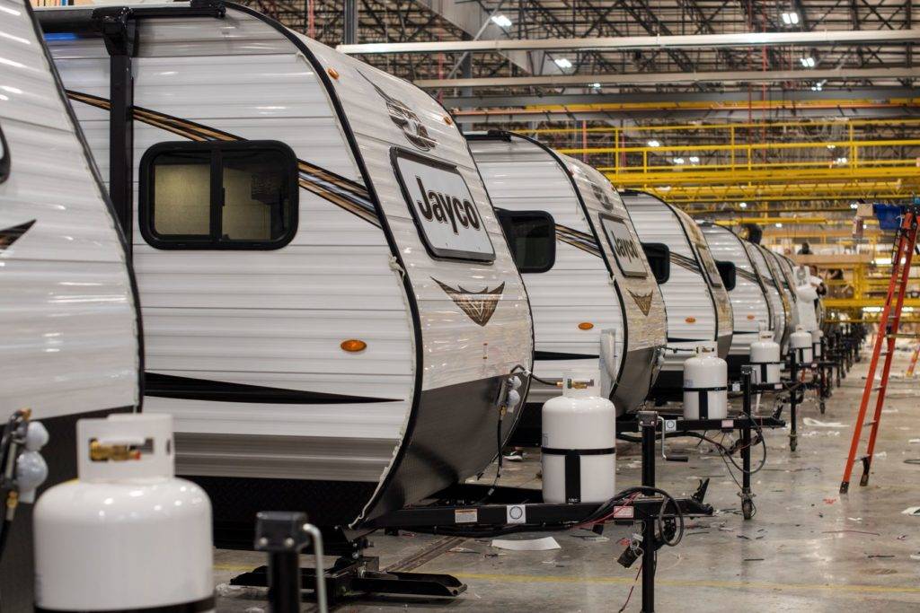 A row of white Jayco RVs with black stripes are parked in a large industrial warehouse