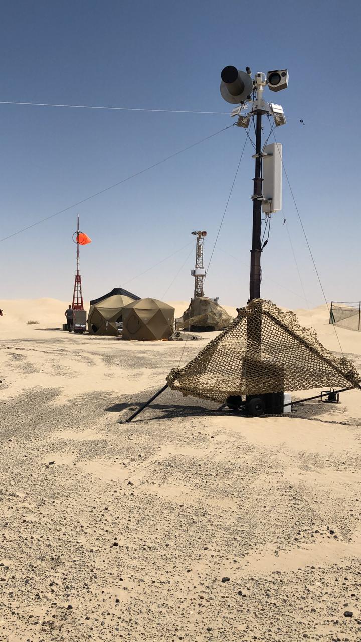 A desert research station with tents, communication towers, and a radar dome