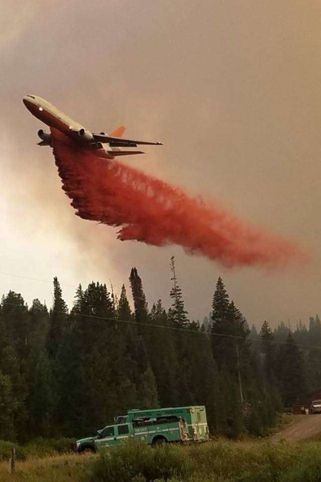 A firefighting plane drops a long plume of red fire retardant over a forest fire