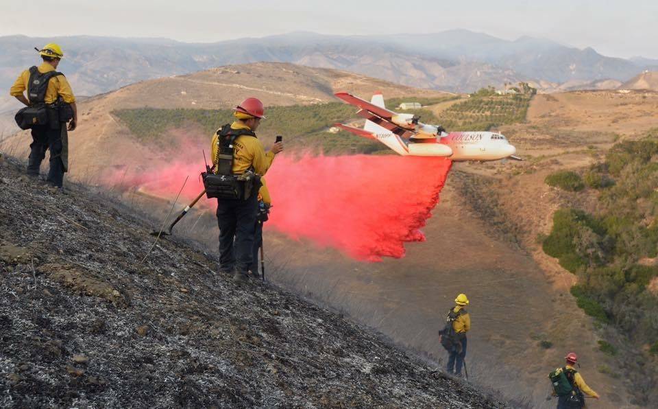 Firefighters use a plane to drop red fire retardant on a hillside blaze