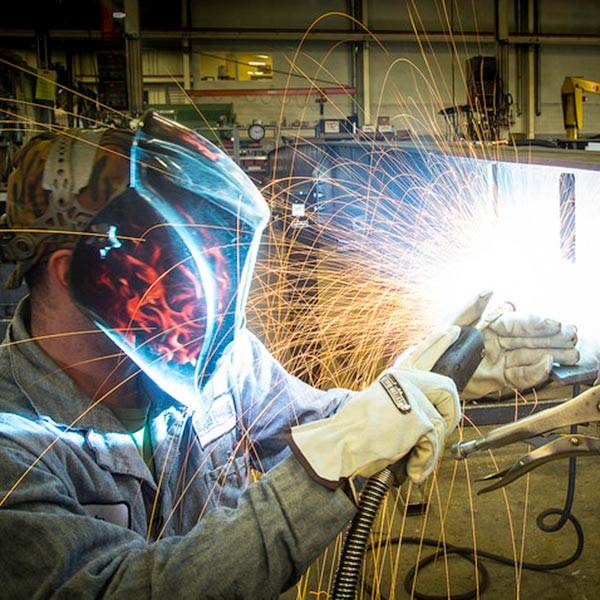 A welder in protective gear is working on a metal piece, creating sparks
