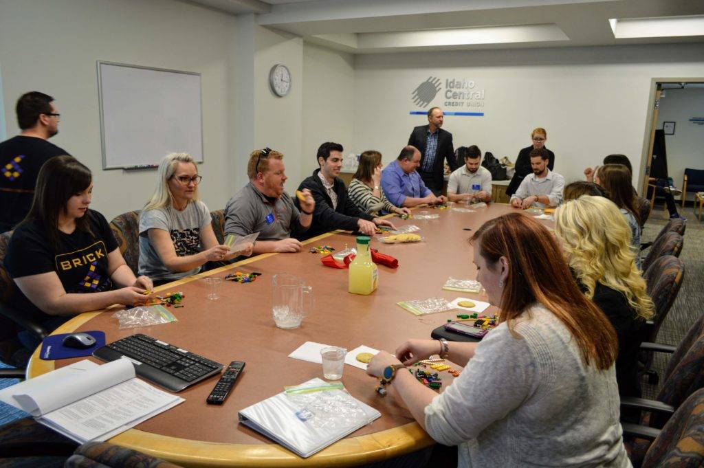 A group of people are gathered around a conference table, engaged in a collaborative activity involving small items and paperwork