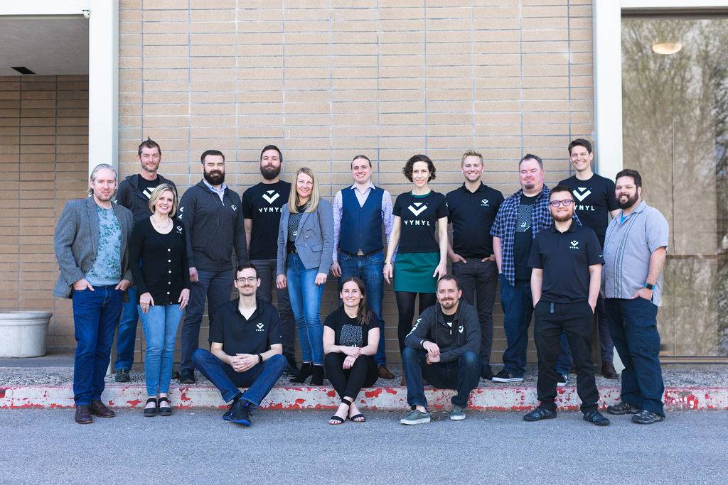 A diverse group of people, mostly wearing black shirts with a logo, pose for a team photo outside a building