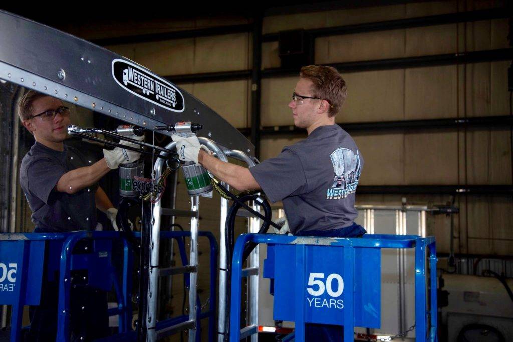 Two mechanics work on a large metal structure in a warehouse setting