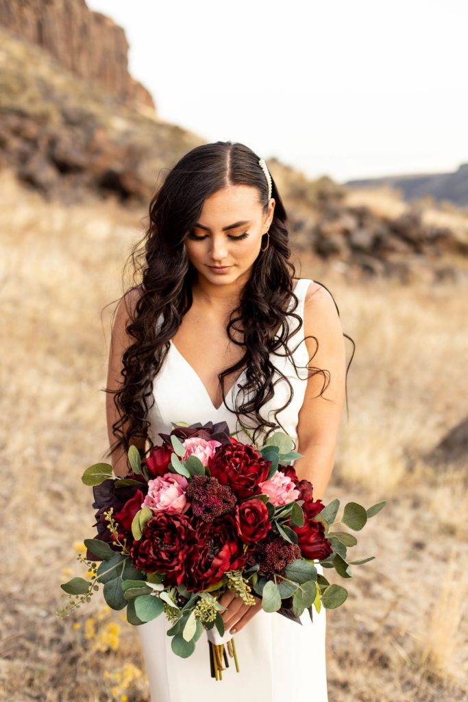 A woman in a white dress holds a bouquet of red and pink roses outdoors