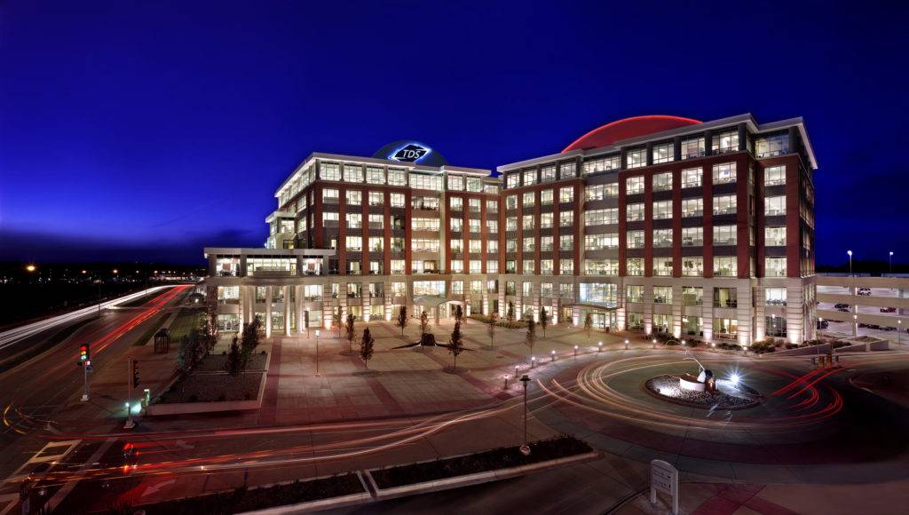 A modern office building complex with a distinctive dome and illuminated at night