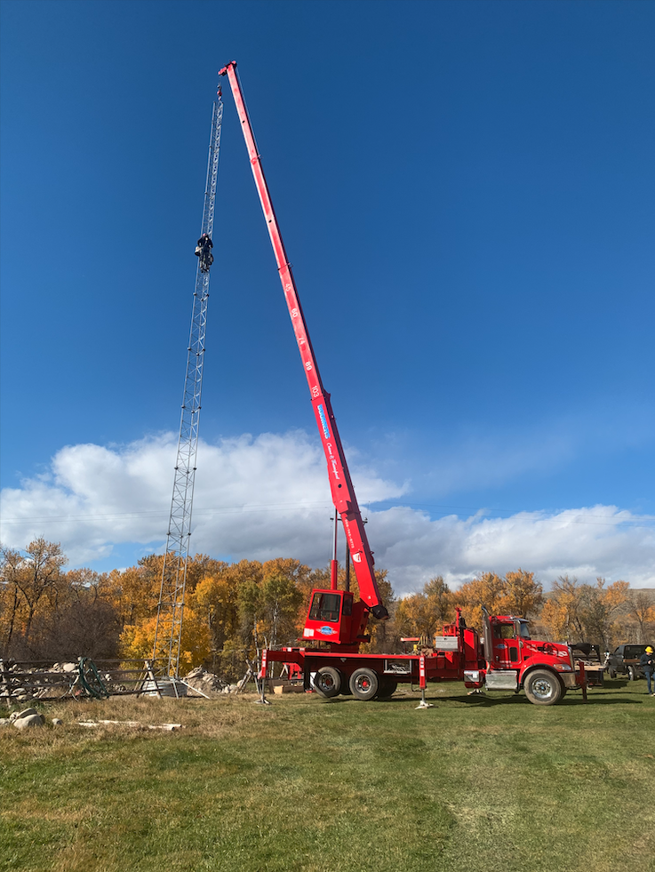 A red crane truck lifts a worker high into the air against a backdrop of autumn trees