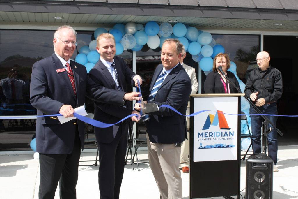 Four men in suits cut a blue ribbon at a grand opening ceremony