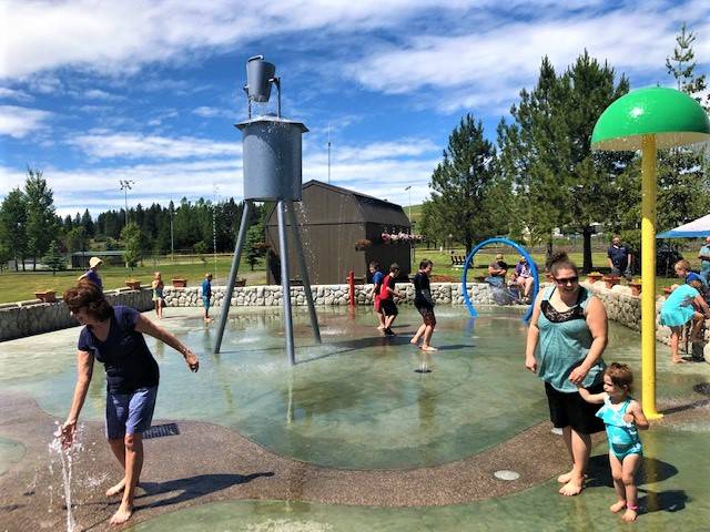People of all ages enjoy a sunny day at a splash pad with various water features