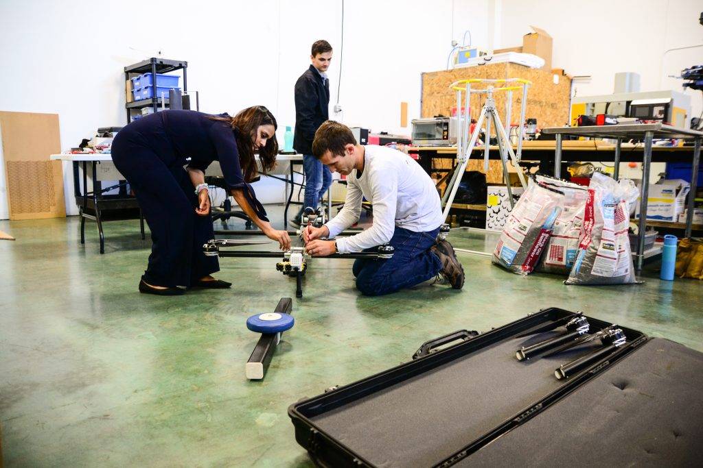 Three people are assembling a drone in a cluttered workshop with tools and equipment
