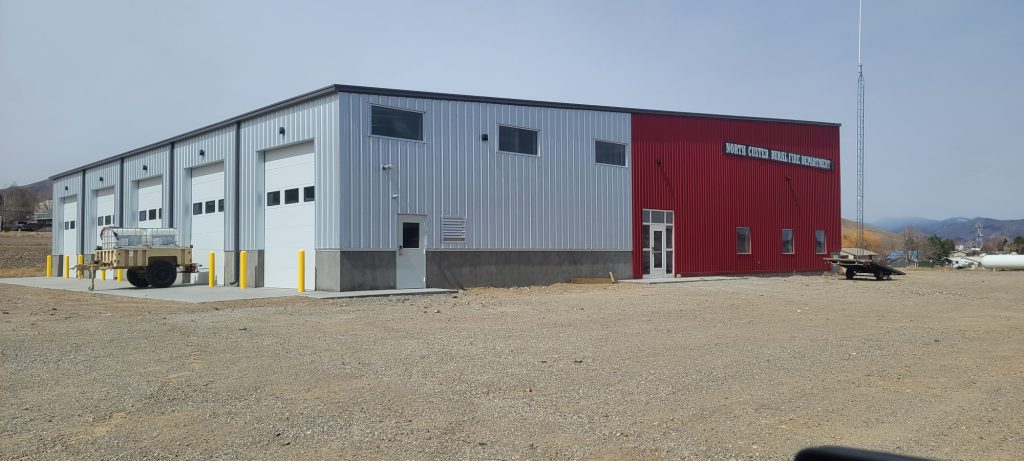 A large industrial building with red and silver siding and four garage doors