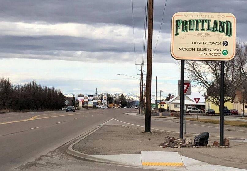 A road sign welcomes visitors to Fruittland, with a cloudy sky and distant mountains in the background
